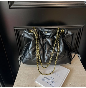 Close-up of black quilted bucket bag with gold chain strap and drawstring closure