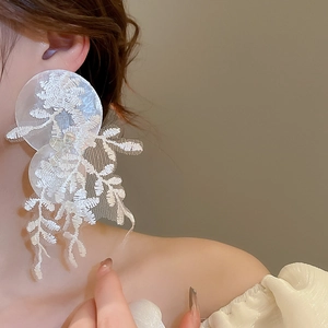 Détail de grandes boucles d'oreilles fleurs en dentelle blanche avec disques de nacre