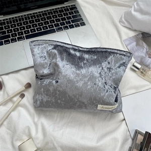 Detail of silver gray velvet makeup bag with logo tag on soft fabric backdrop