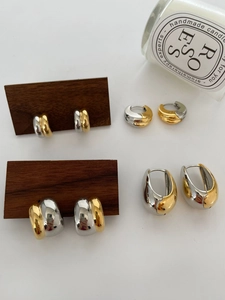Detailed view of mixed gold and silver teardrop C-shape earrings on wooden display