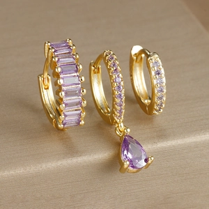 Macro shot of three-piece gold drop earrings set with purple rhinestones on silk surface