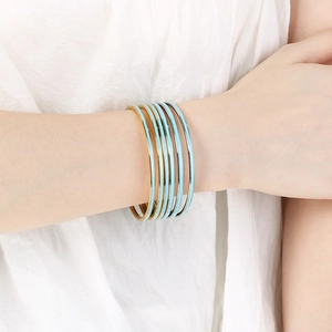 Detail of stacked blue enamel bangles with gold edges on white fabric background