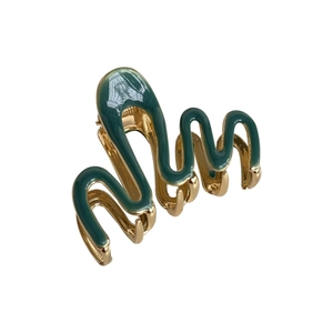 Pinza per capelli ondulata in metallo dorato con smalto verde scuro su sfondo bianco