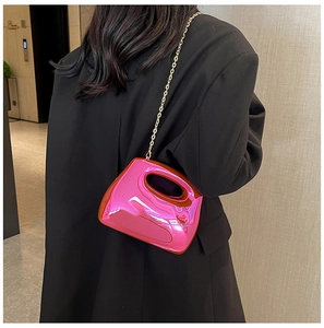 Detailed close-up of pink mirror acrylic evening bag with gold chain strap on black blazer