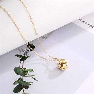 Detail view of a gold-tone necklace with a hollow heart pendant and white inlay on paper