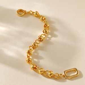 Minimalist gold plated metal knot chain bracelet with rectangle clasp in warm lighting
