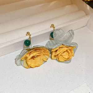 Detail view of yellow fabric flower earrings with green bead on a textured jewelry box