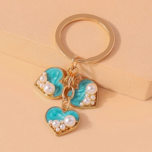 Close-up of golden heart pendants with turquoise enamel and pearls on a sleek keychain