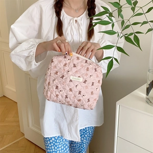 Détail d'une trousse à maquillage matelassée rose avec motif d'ours tenue par un mannequin