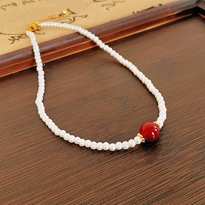 Détail du collier de perles plaqué or 18 carats avec une perle rouge sur bois