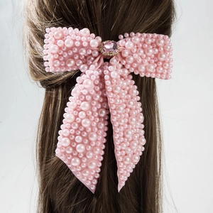 Detailed macro view of a pink bow hair clip with pearls and gemstones on brown hair