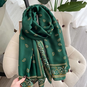 Elegante sciarpa in seta verde scuro con motivo paisley dorato drappeggiata su sedia