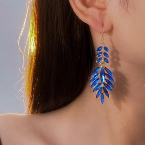 Detailed close-up of blue leaf-shaped crystal tassel earrings on model with golden finish