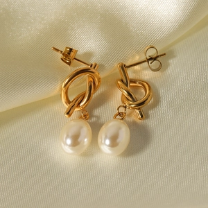 Baroque pearl drop earrings with golden knot design on elegant silk fabric background