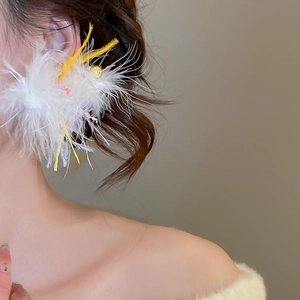 Close-up of white feather pendant earrings with golden bead and soft pink highlights