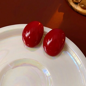 Deep red enamel pebble earrings with silver needles and glossy finish on neon white tray