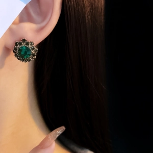 Close-up of vintage flower stud earring with emerald green stone and black crystals