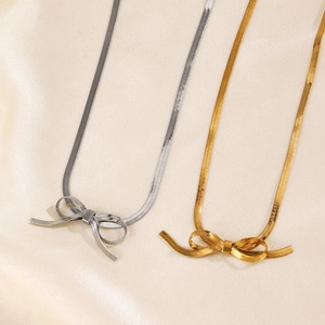 Gold and silver bow pendant necklaces featuring sleek snake chain on satin background