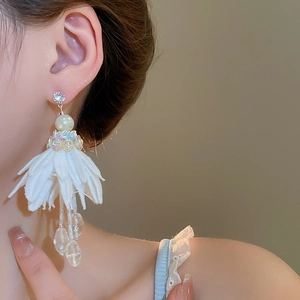 Close-up of white chiffon flower earrings with rhinestones, pearls, and beaded tassels