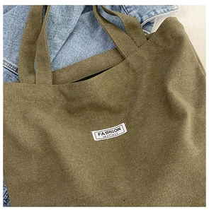 Detail of army green canvas tote bag with a white fashion label on denim background