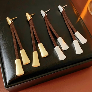 Detail view of gold and silver retro tassel earrings with dark brown leather cords