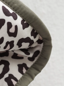 Close-up of leopard print fabric with olive green edge stitching on a winter jacket