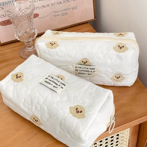 Detail of white quilted bear embroidery makeup bags in two sizes on wooden surface