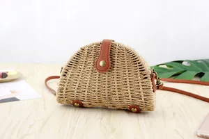Detail view of semi-circular straw crossbody bag with brown leather base and rivets