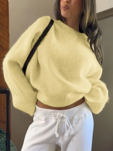 Detailed knit texture of loose pale yellow long-sleeve sweater on model indoors