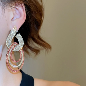 Detailed view of elegant gold drop earrings featuring pink and white rhinestone concentric rings