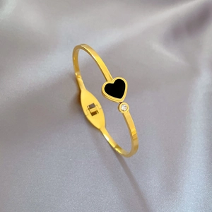 Detail of gold heart bangle with black inlay and white zircon on silk background