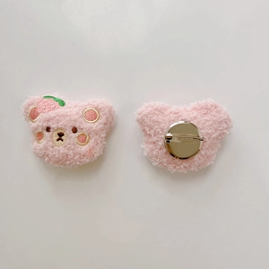 Detailed view of pink plush bear brooch showing strawberry embroidery and metal pin back