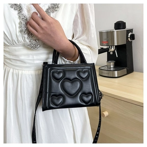 Détail du sac à main noir avec texture cuir à motifs cœurs 3D et poignée supérieure