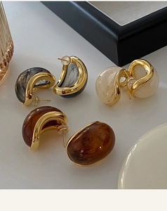 Detail of C-shaped resin earrings in marble and amber colors with gold plating