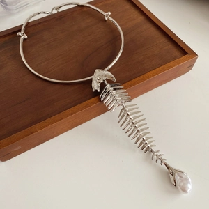 Close-up of silver fishbone pendant with baroque pearl on a rigid metal choker necklace