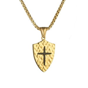 Vintage gold shield pendant necklace with black cross and textured finish on white background