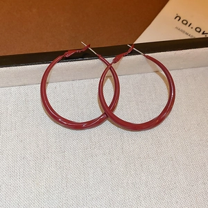 Gros plan de grandes créoles en émail rouge foncé avec placage à l'or sur tissu blanc