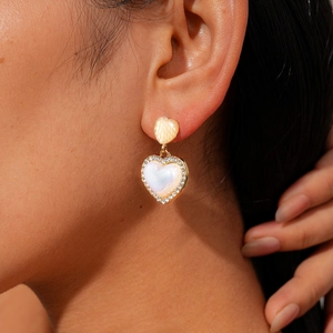 Detail of model wearing double gold heart earrings with white inlay and shimmering rhinestones