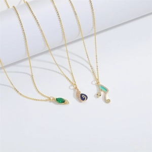 Three gold-plated necklaces with green leaf, blue drop, and snake zircon pendants on white podiums
