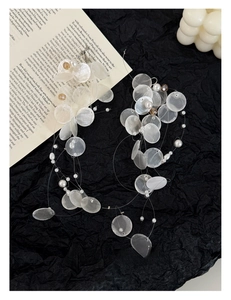 Artistic layout of shell and pearl tassel necklace on black texture and book pages