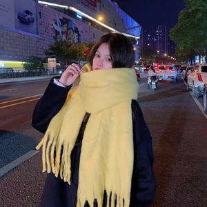 Detailed view of soft yellow mohair scarf with tassels shown in a city street night view