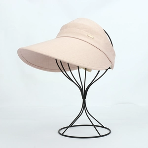 Detail of light pink sun visor with wide brim and elegant gold metal logo plate
