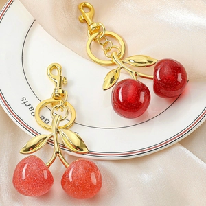Detail of red glitter cherry keychains with gold leaves on champagne silk fabric