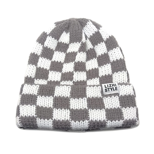 Close-up of checkerboard knitted beanie with gray and white pattern and textile label