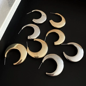 Detailed view of C-shaped metal hoop earrings in gold and silver with polished finish