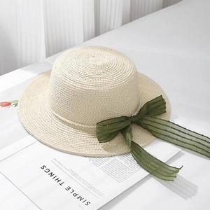 Elegant beige raffia sun hat with pearls and green ribbon on a white background