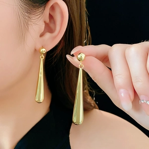 Detail view of long golden metal waterdrop earrings worn to show size and drop length