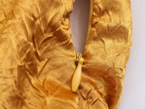 Detail van gouden satijnen stof met geplooide textuur en onzichtbare ritssluiting