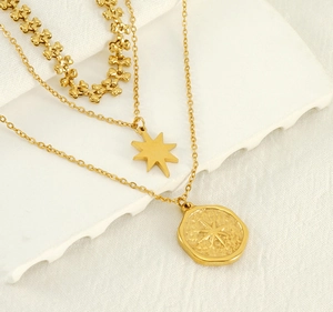Macro detail of layered gold necklaces with star pendant and hammered disc on white fabric
