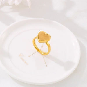 Minimalist gold heart stainless steel ring placed on a white ceramic jewelry dish